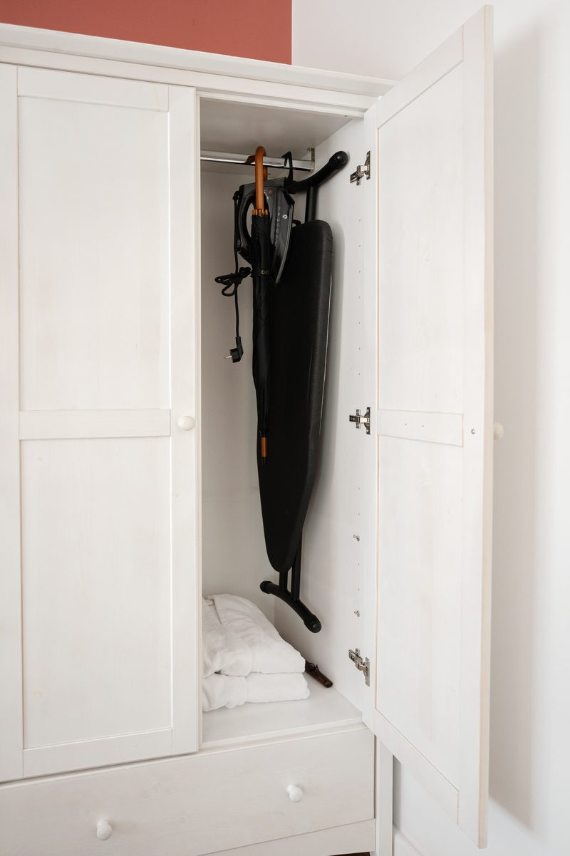 Ein offener Kleiderschrank mit Bademänteln, einem Bügelbrett und einem Regenschirm