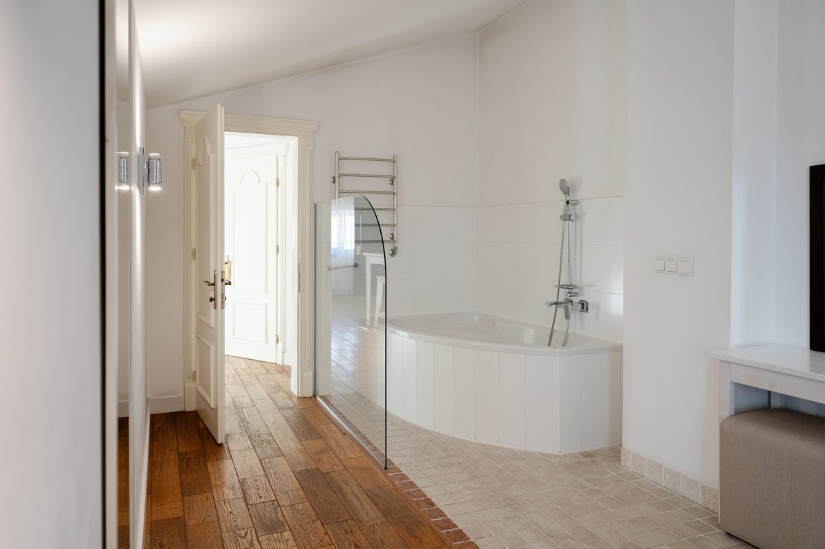 Die Eckbadewanne hinter einer Glaswand, mit offenen Türen zum Flur