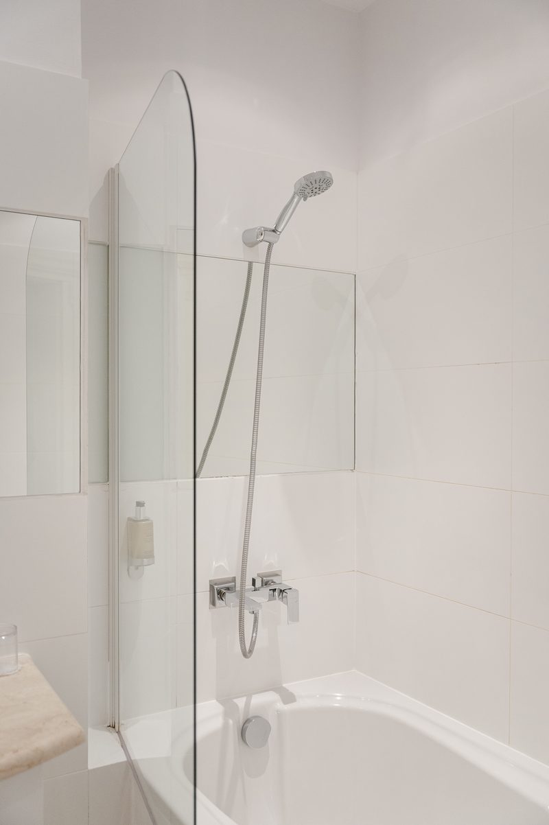 Eine Badewanne mit Handbrause hinter einer Glaswand