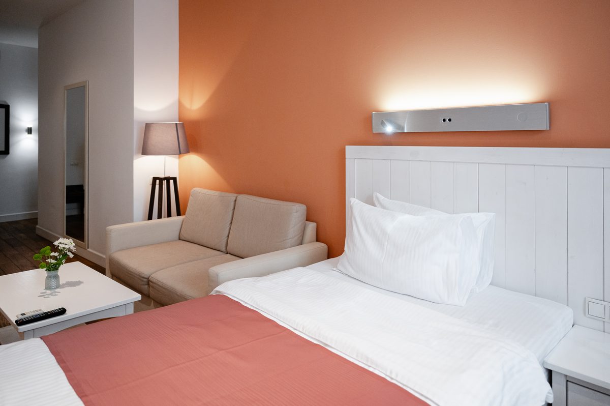 Studio: die Betten, ein Sofa und eine Stehlampe vor einer korallenroten Wand